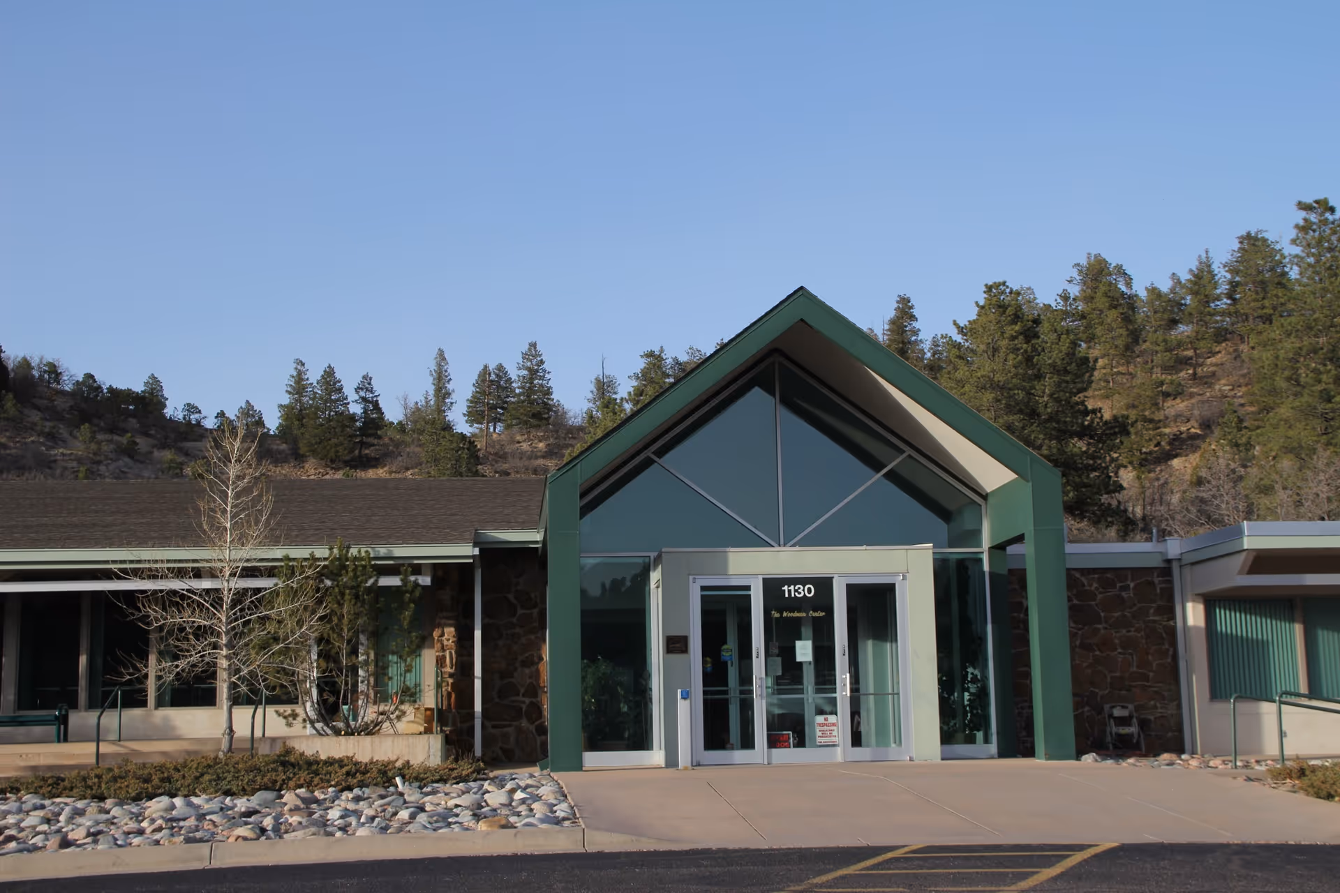 Front view of a modern facility entrance with glass doors, green framework, and stone walls.