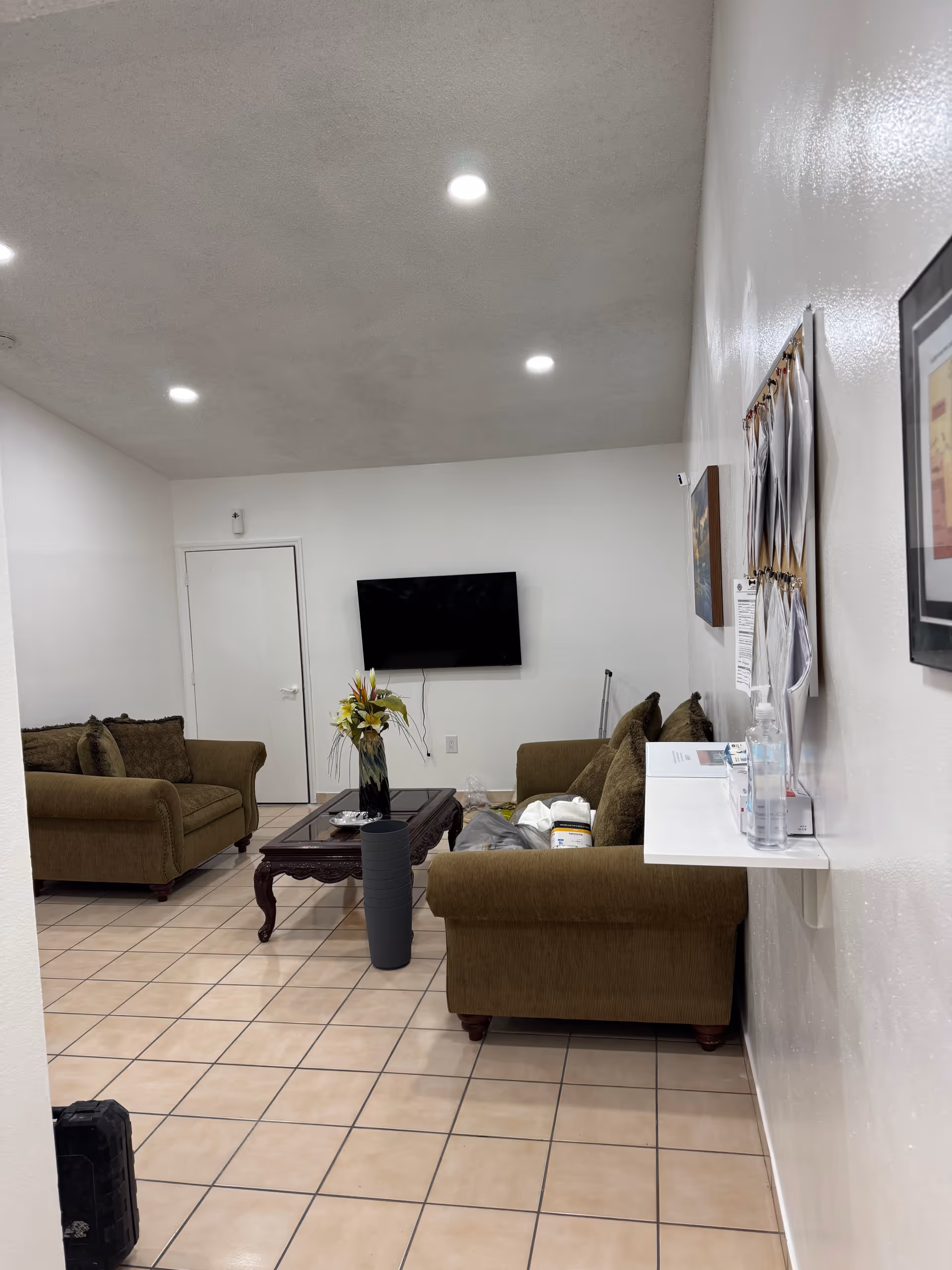 A senior living facility living room with brown sofas, a coffee table, and wall TV.