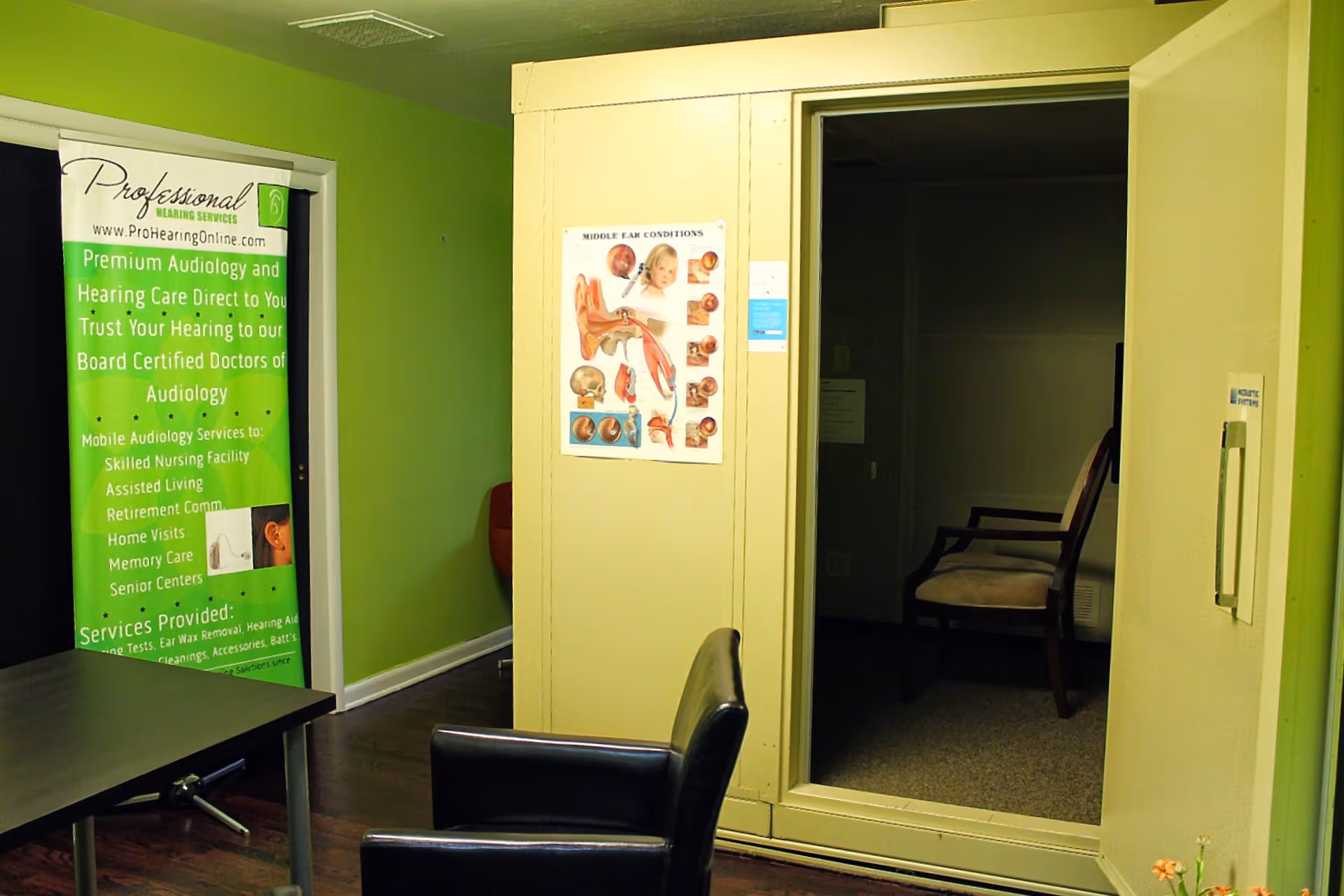 Green-walled reception area with a hearing services banner and seating near a doorway.