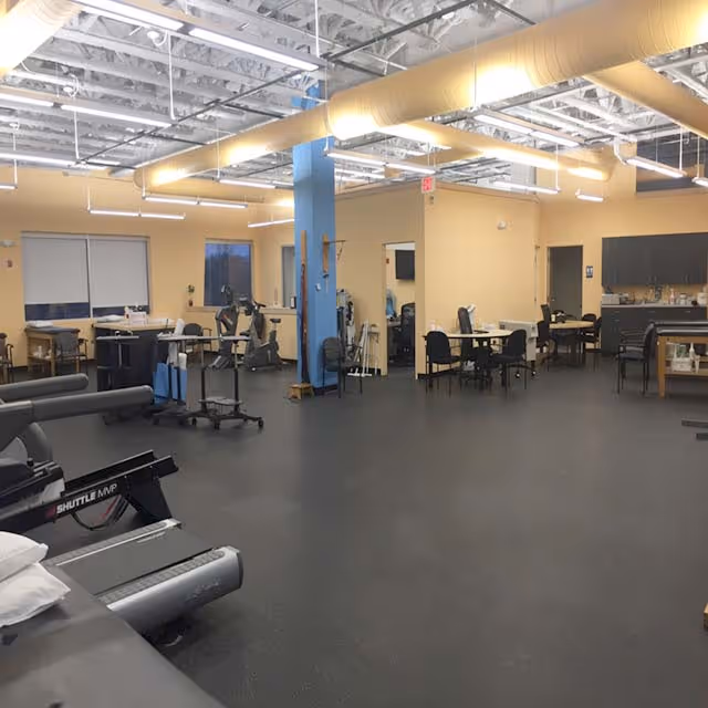 Therapy gym interior with exercise equipment, tables, chairs, and blue columns.