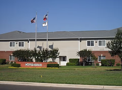 Two flagpoles flank a beige Garden Estates building with a manicured lawn and sign.