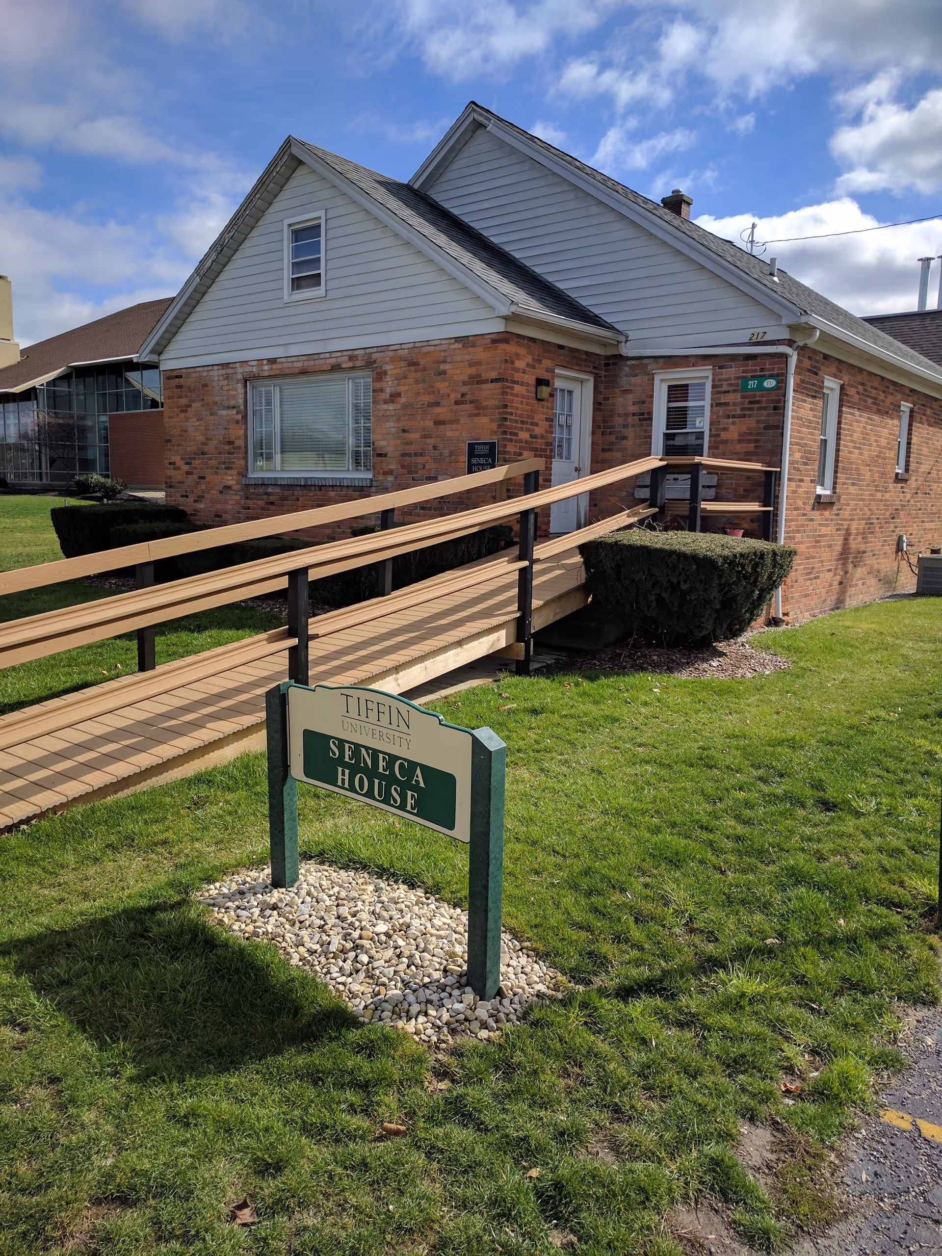Brick assisted-living building with wooden ramp and Seneca House sign in front yard.