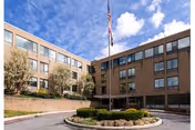 Exterior of a four-story brick senior living facility with flagpole and manicured landscaping.