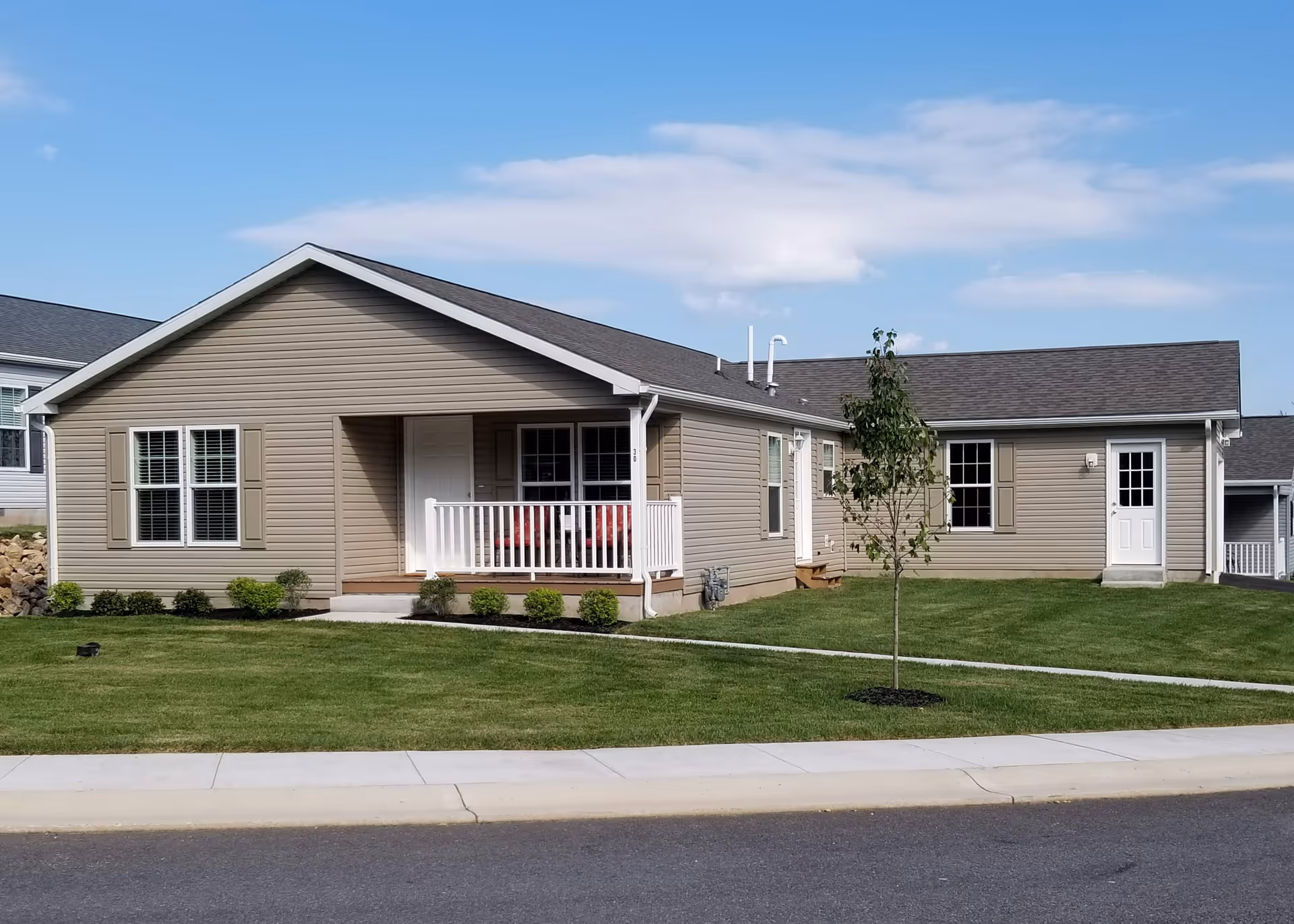 Single-story beige senior living building with a small porch and manicured lawn.