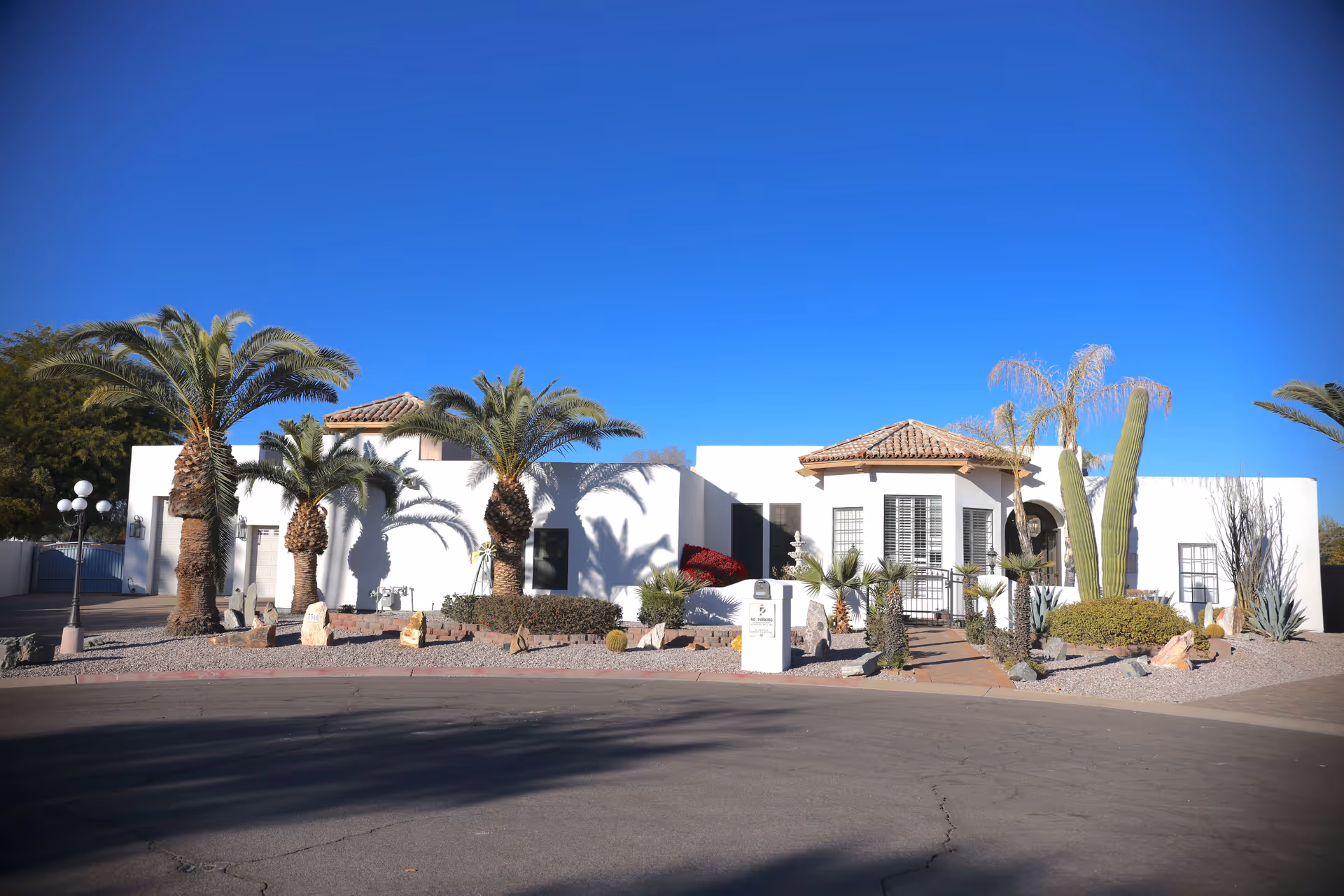 Sunlit, modern senior living facility facade with white walls, palm trees, and desert landscaping.