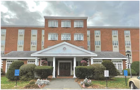 Brick senior living facility with columned entrance and manicured shrubs at Buckley-Greenfield Healthcare Center.