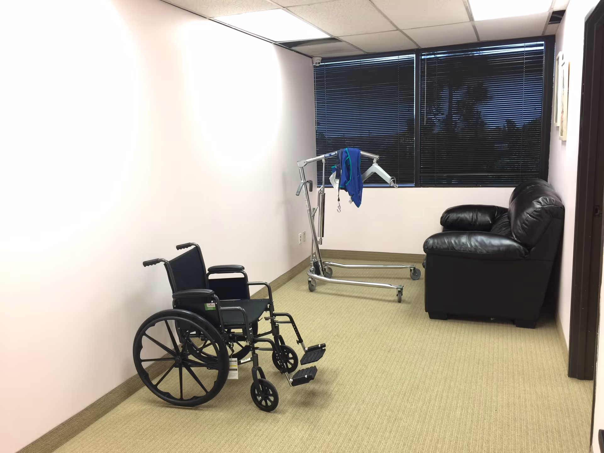 Wheelchair, patient lift, and black sofa in a small empty indoor corridor.
