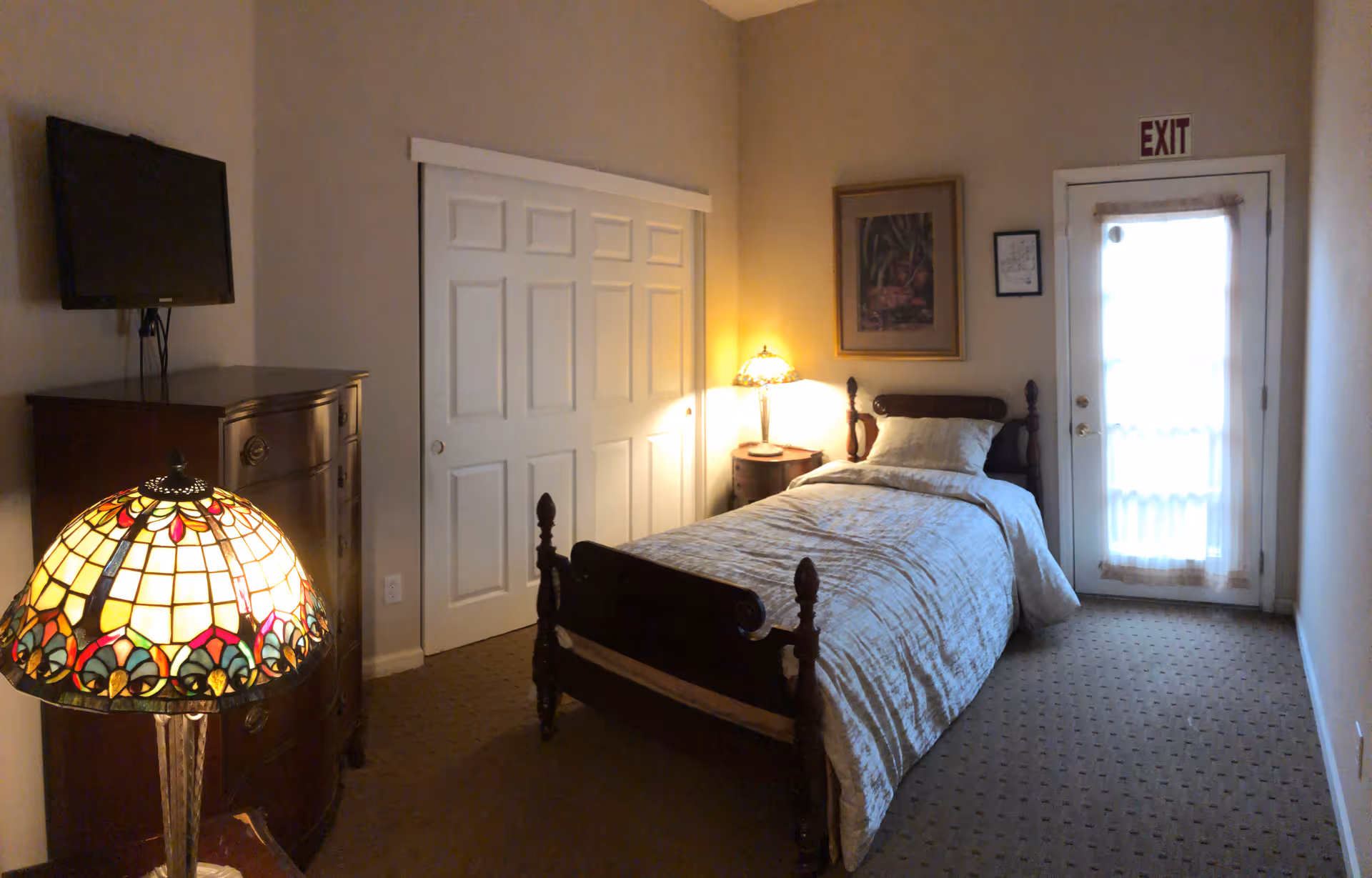 Cozy bedroom with a wooden bed, dresser, lamp, and exit door.