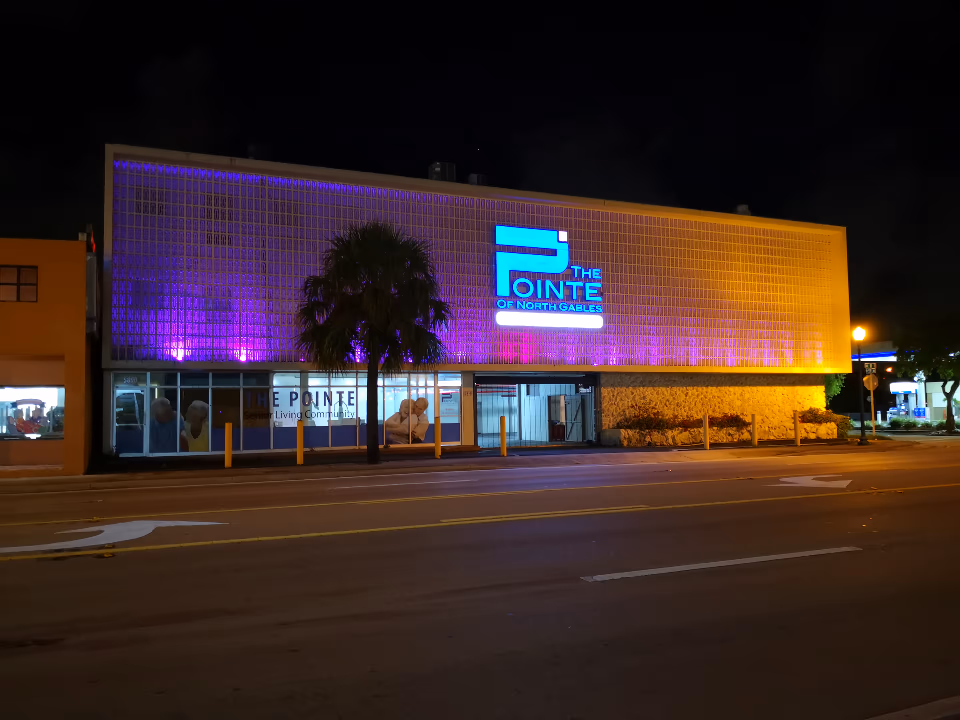 Night view of Pointe North Gables exterior with purple-lit facade and glass entrance.