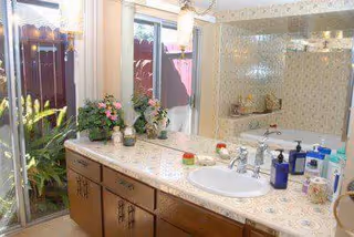 Bathroom vanity with a sink, patterned countertop and wooden cabinets, mirror, toiletries, potted plants, and a sliding glass door opening to an outdoor garden.