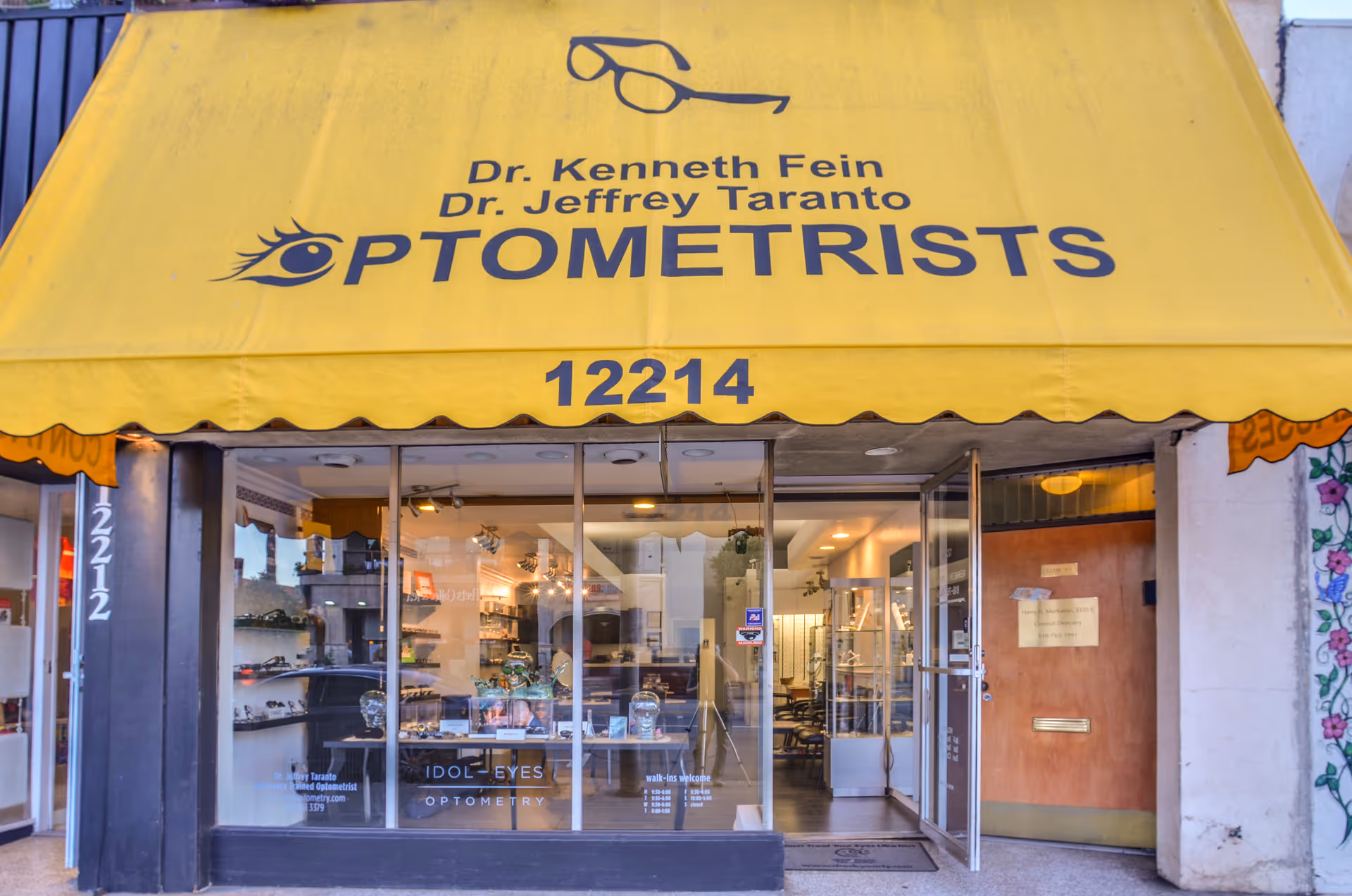 Bright storefront with a yellow awning reading OPTOMETRISTS and glass entrance doors.