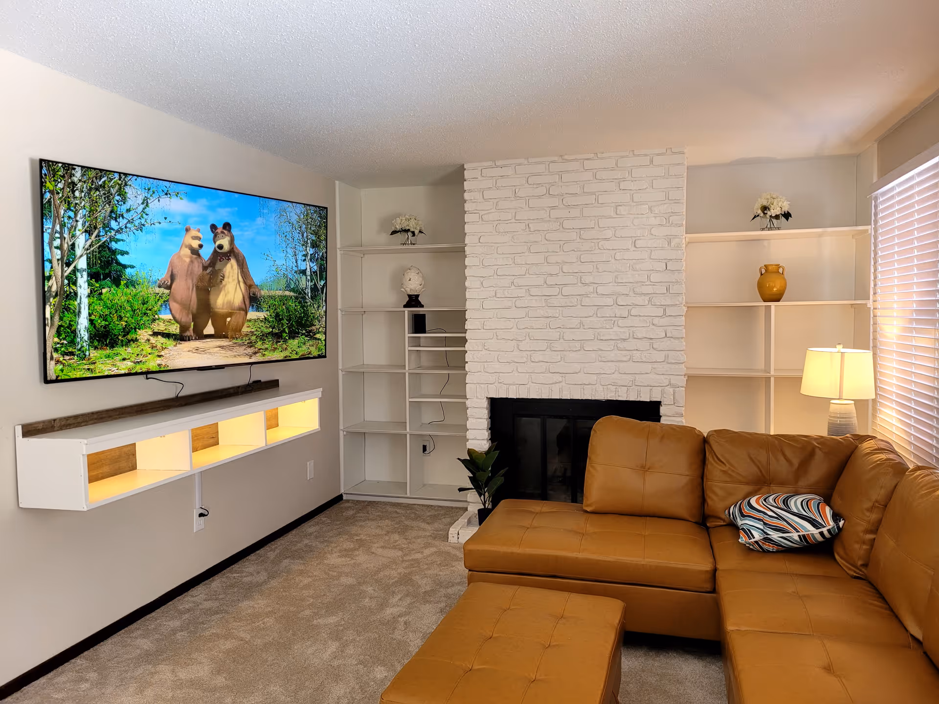 Living room with tan sectional, white brick fireplace, and mounted TV.