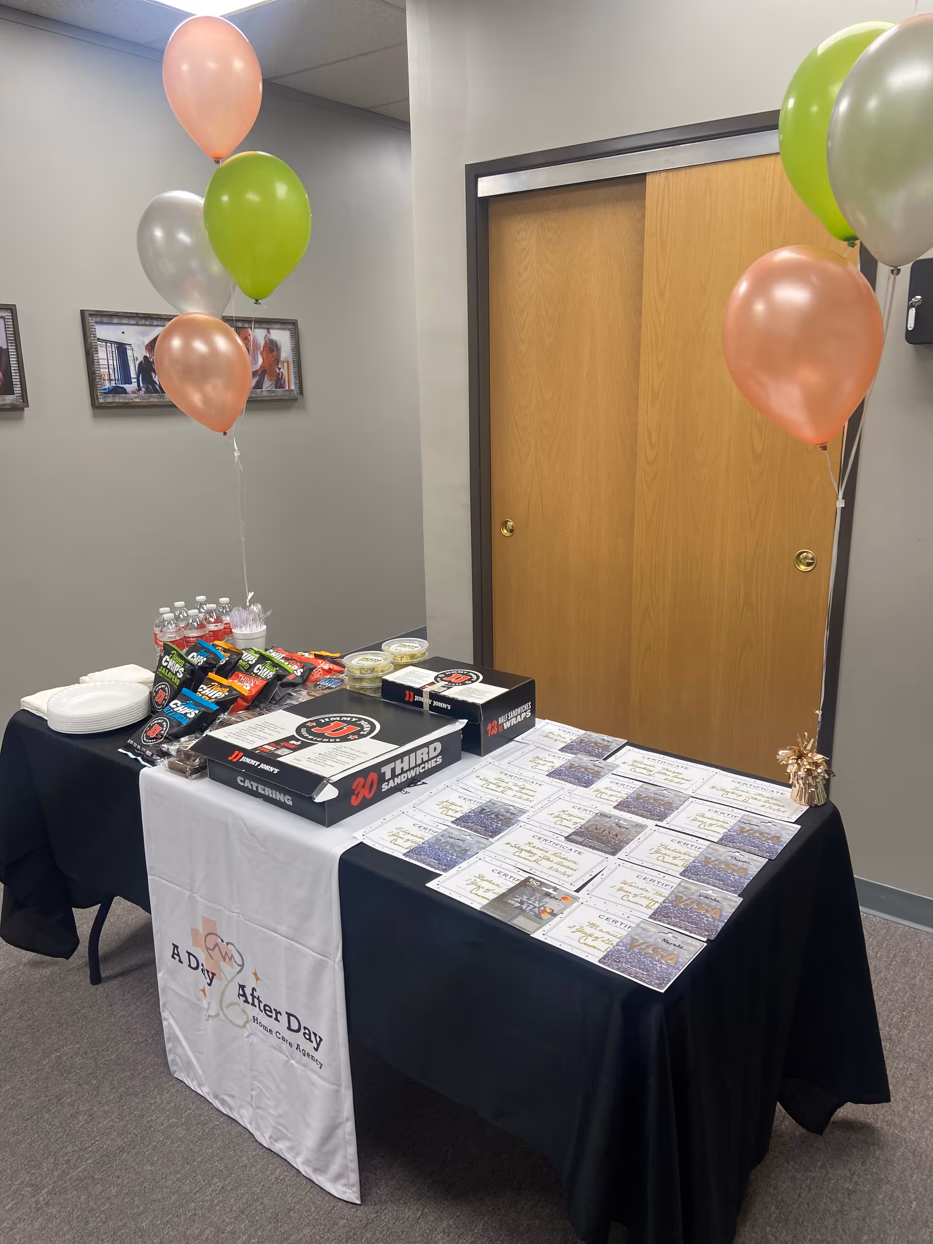 Table with balloons, catering boxes, water, and brochures in a senior care facility interior.