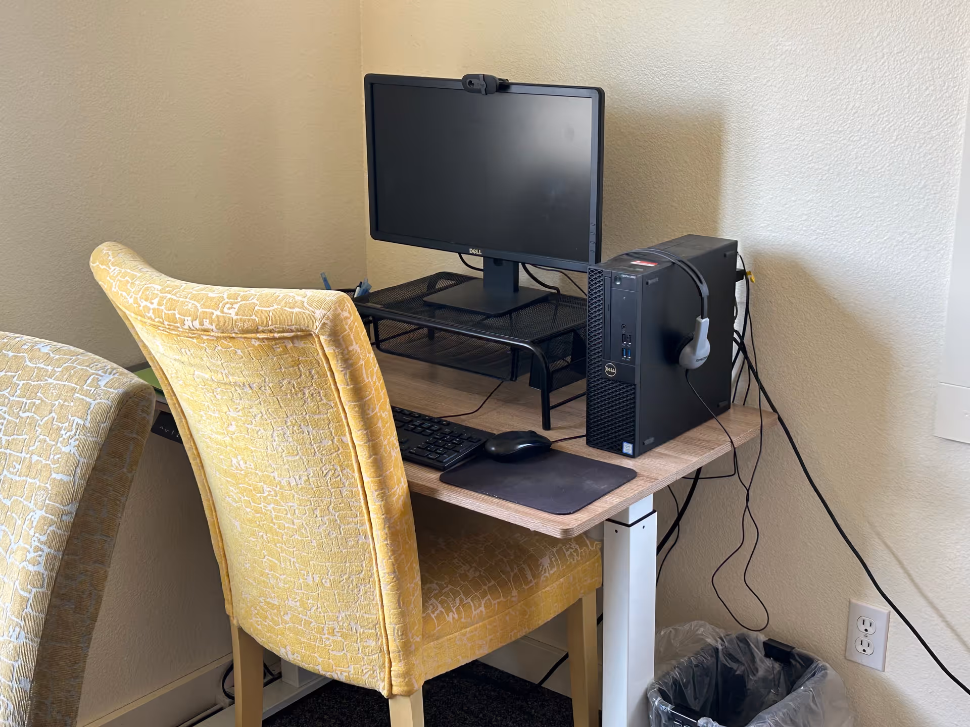 Desk setup with monitor, keyboard, mouse, headset, and a yellow upholstered chair.