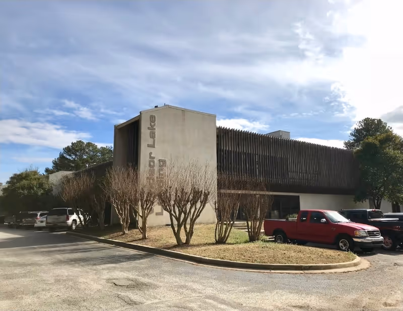 Exterior view of a low-rise facility with parking, trees, and a clear blue sky.