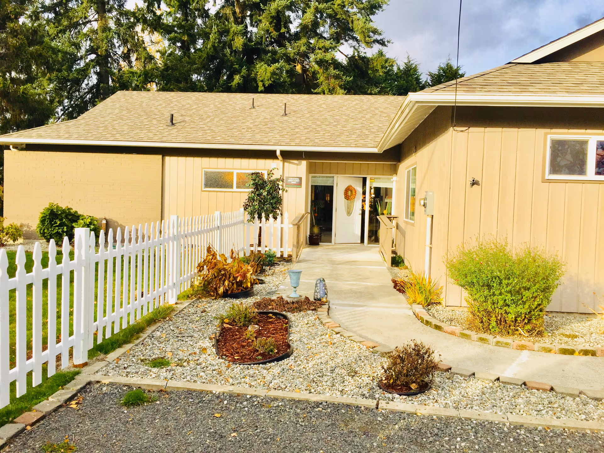 Front entrance of a beige senior living facility with a white picket fence and pathway.
