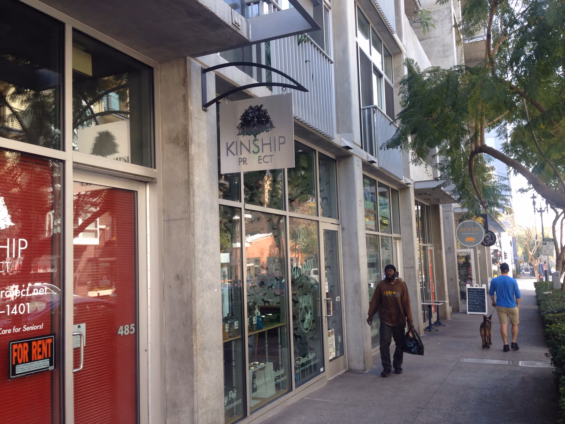 Exterior city street with Kinship Project storefront and pedestrians walking by.