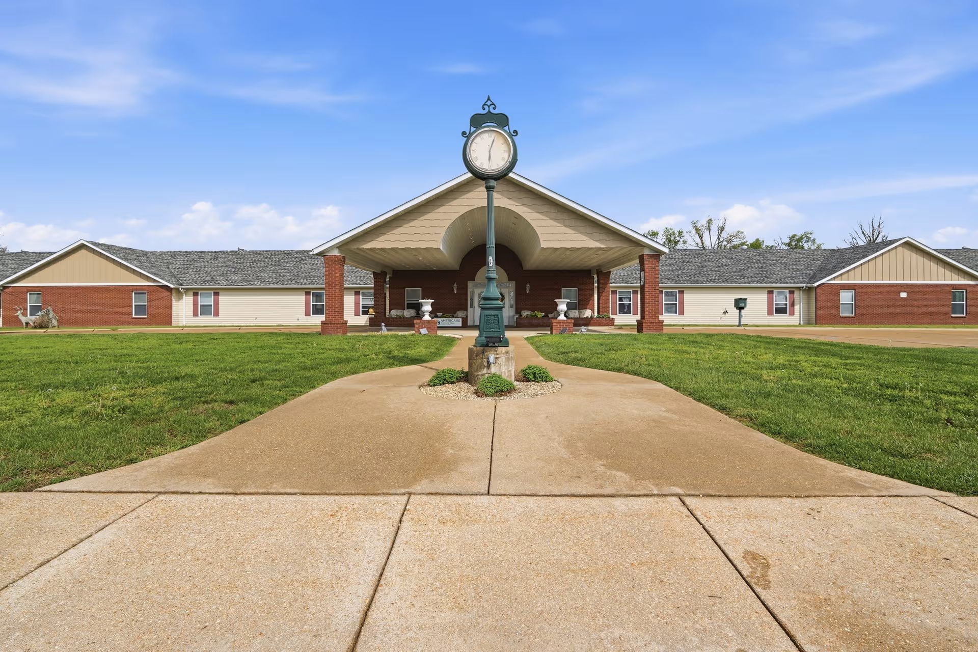 Wide view of Victorian Place of Owensville entrance with clock, lawn, and walkway.