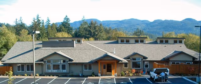 Single-story PeaceHealth Whatcom Hospice building with entrances, parking, and mountains in background.