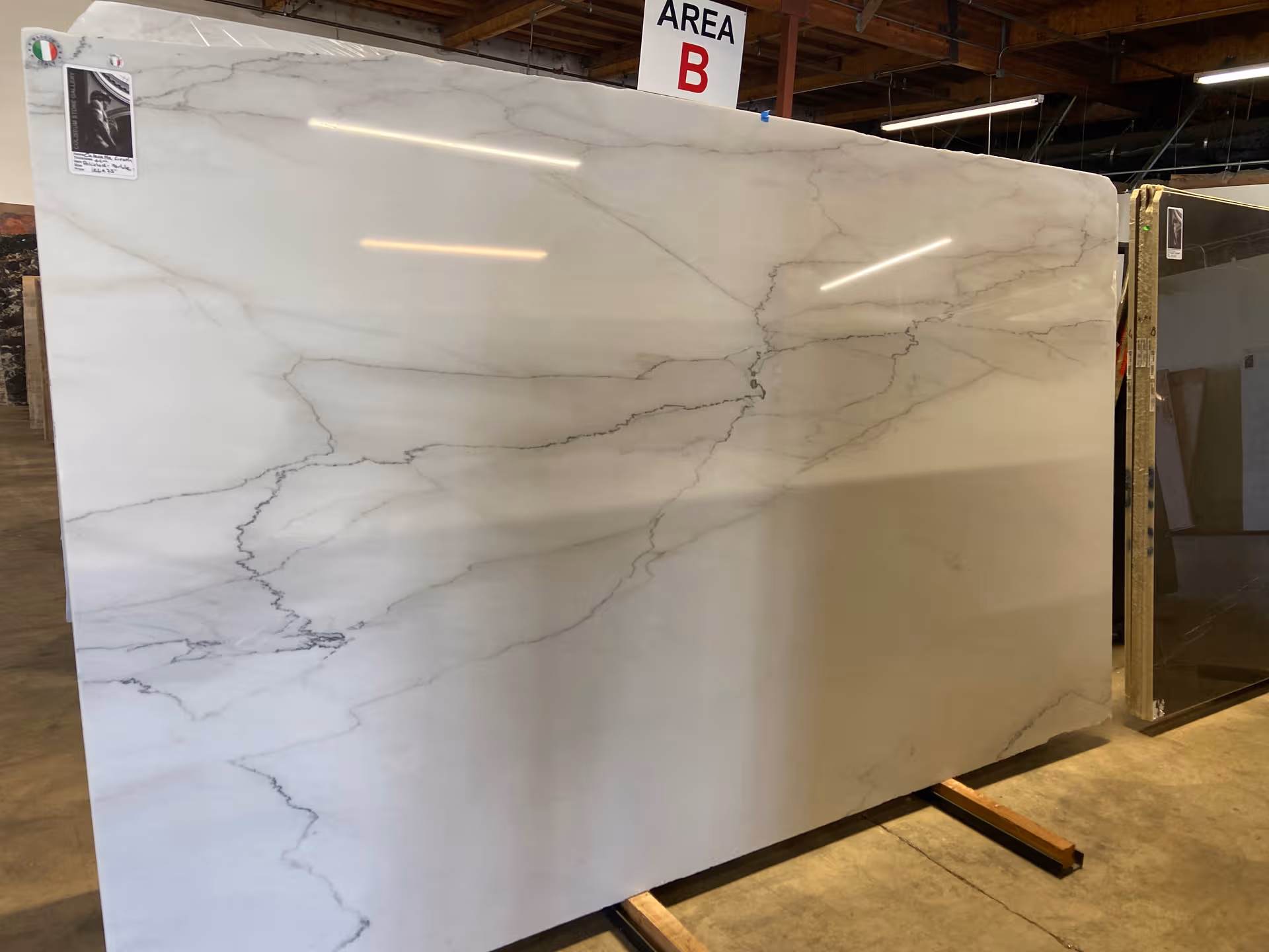 A large marble slab is displayed in a warehouse, with an area sign and wooden supports.