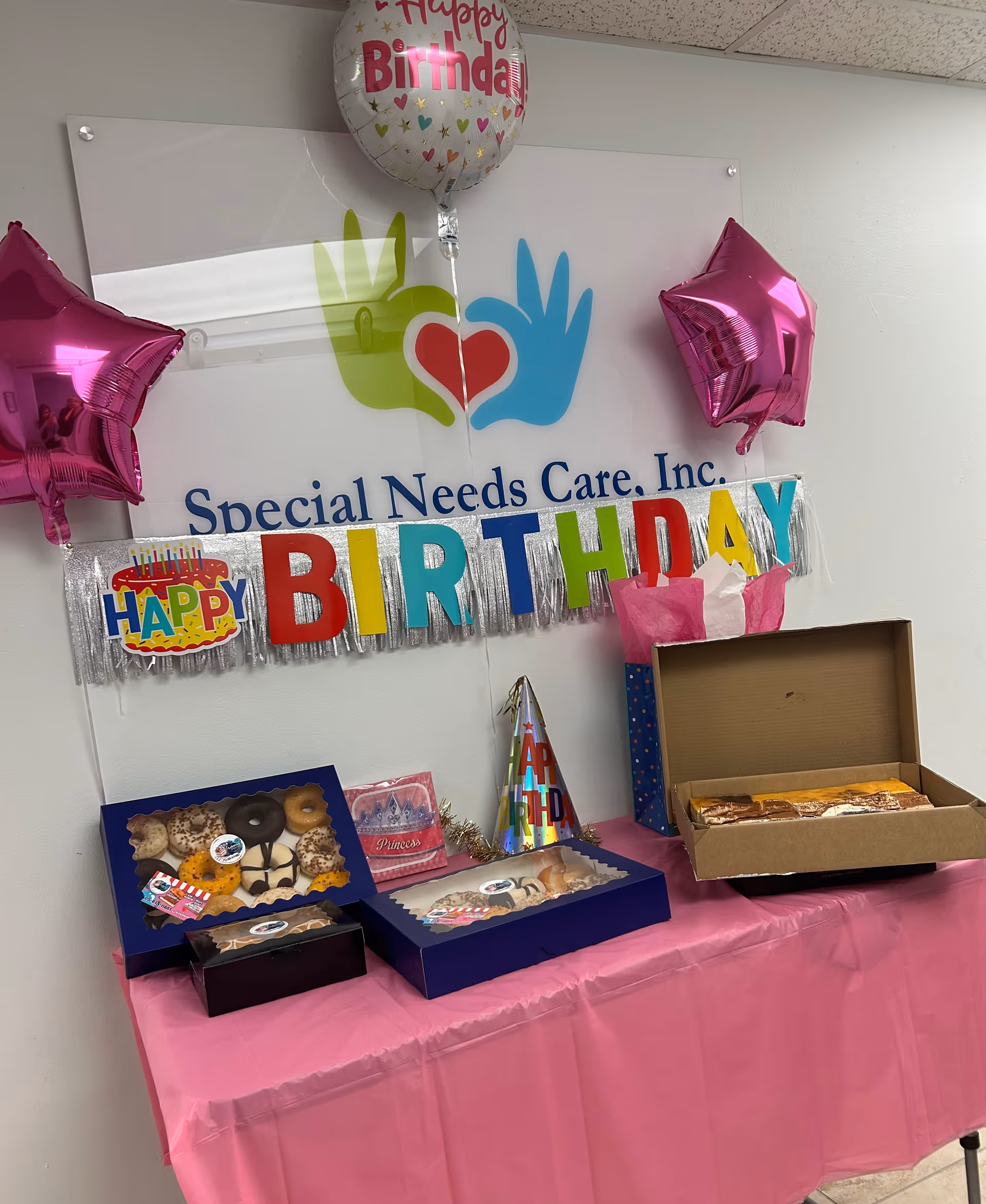 Birthday setup at Special Needs Care Inc with banner, balloons, and desserts on pink table.