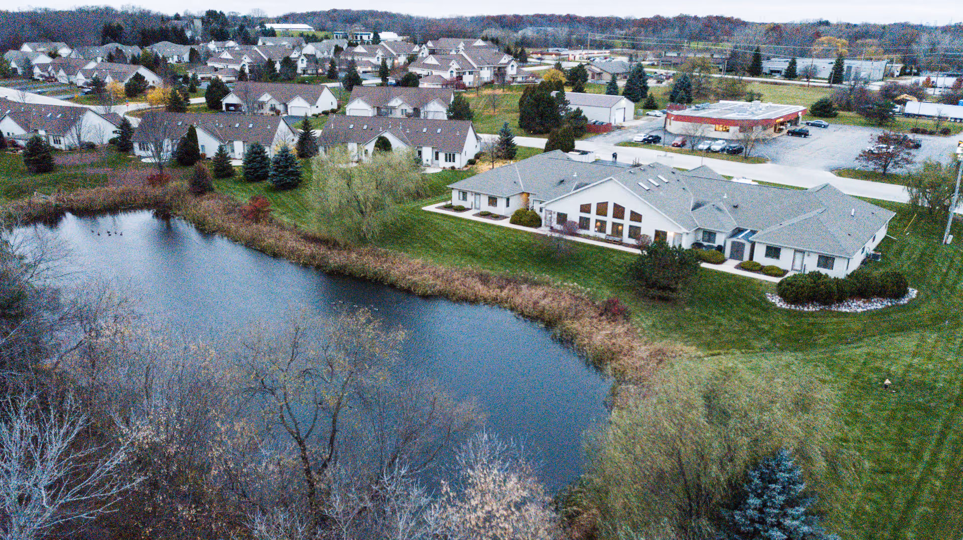 Aerial view of the assisted living building beside a pond with surrounding lawns and nearby houses.