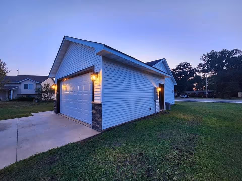 Residential-style exterior of a light-blue building with garage doors and outdoor lights.