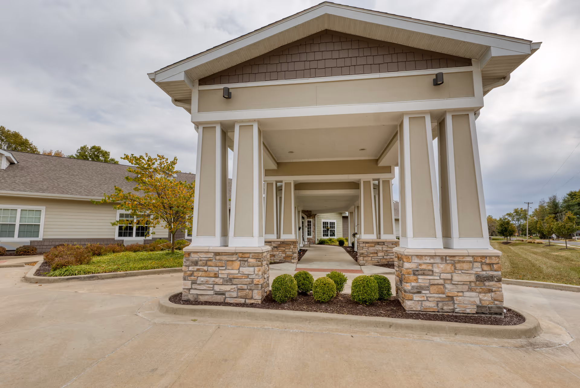 Covered porte-cochère entrance with columns, stone bases and landscaping at the front of a senior living building.