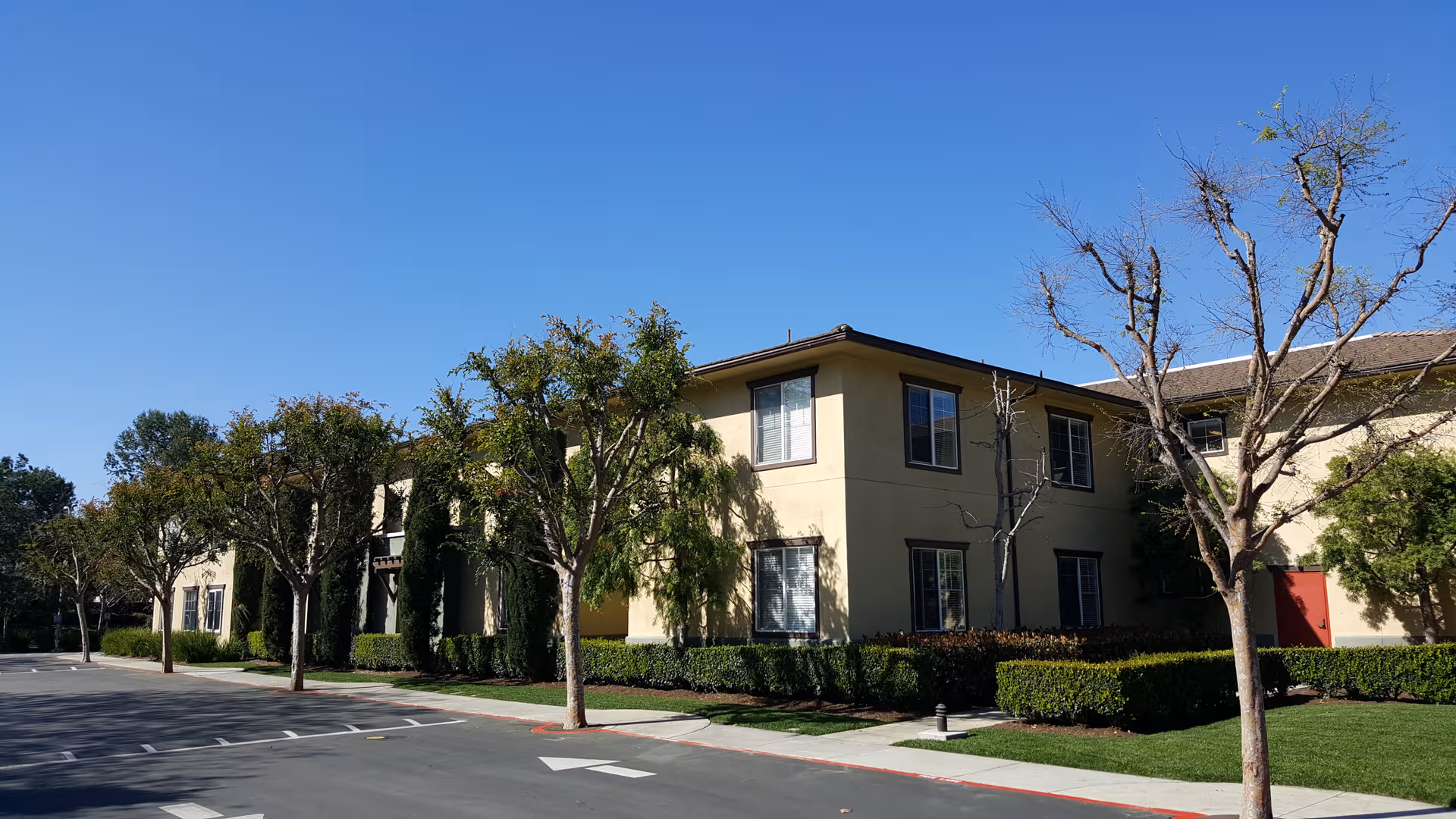 Exterior view of Woodbridge Terrace senior living building with trees, shrubs, and a parking lot.