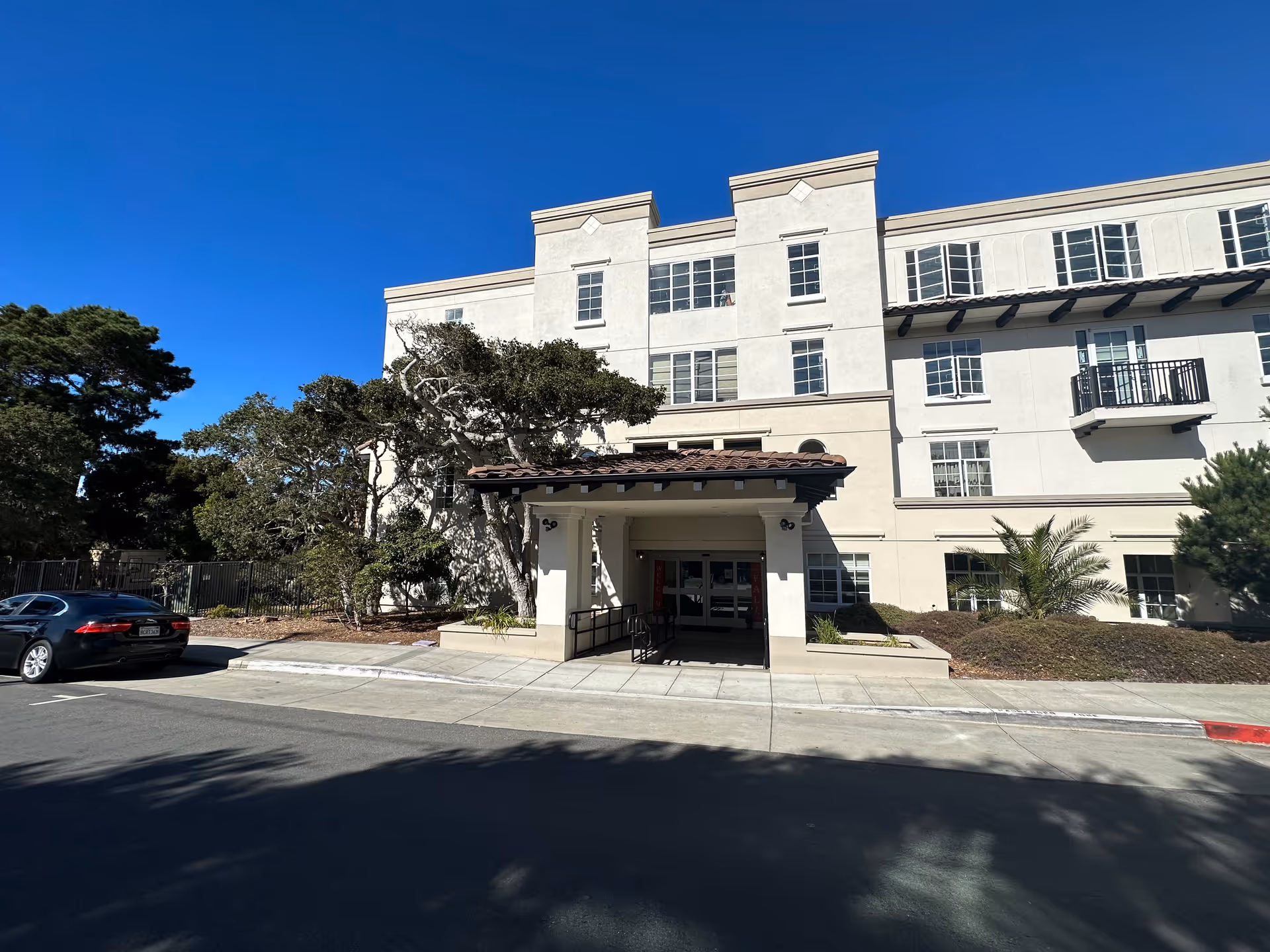 The front entrance of a senior living facility surrounded by greenery and a clear blue sky.