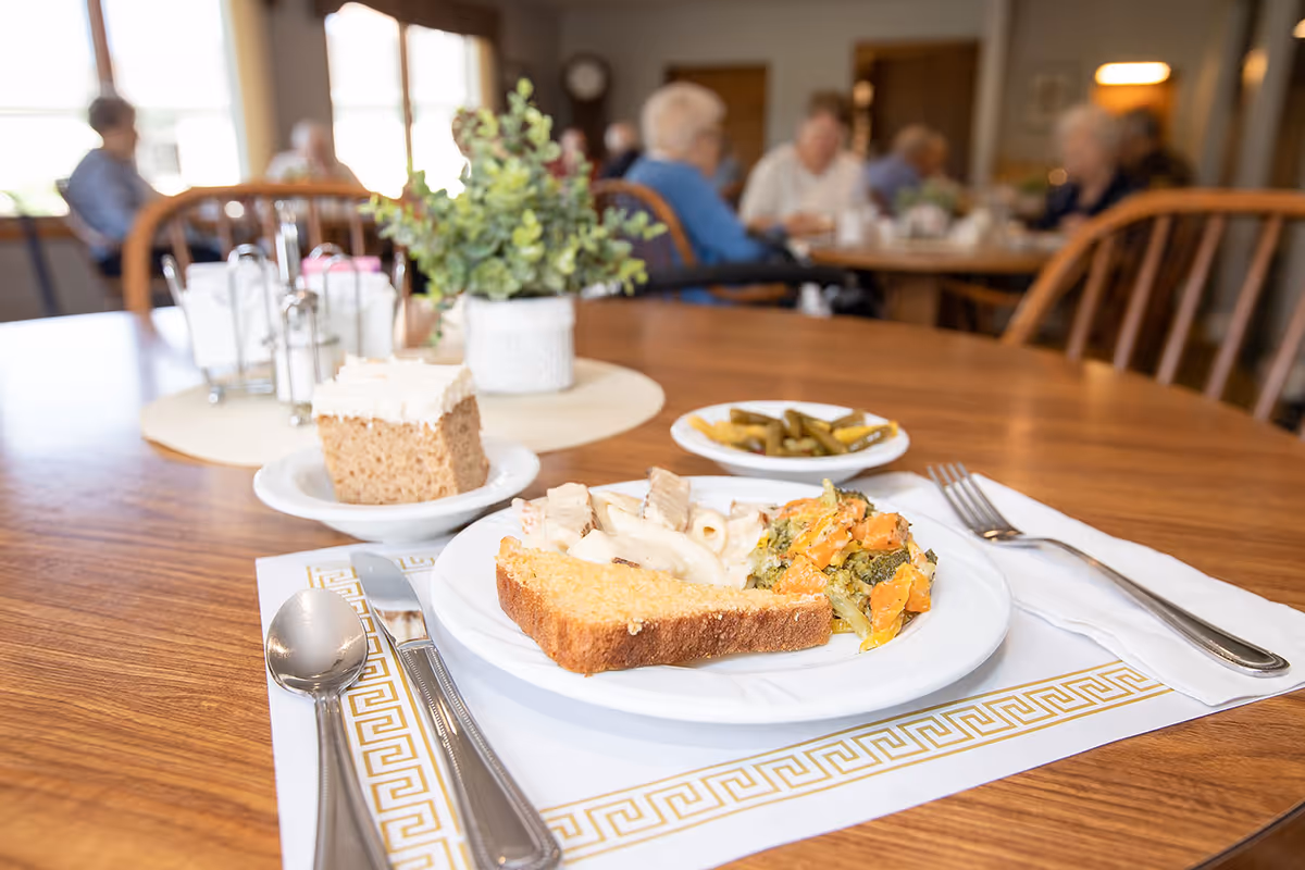 A dining table with plated meals in a busy senior living dining room.