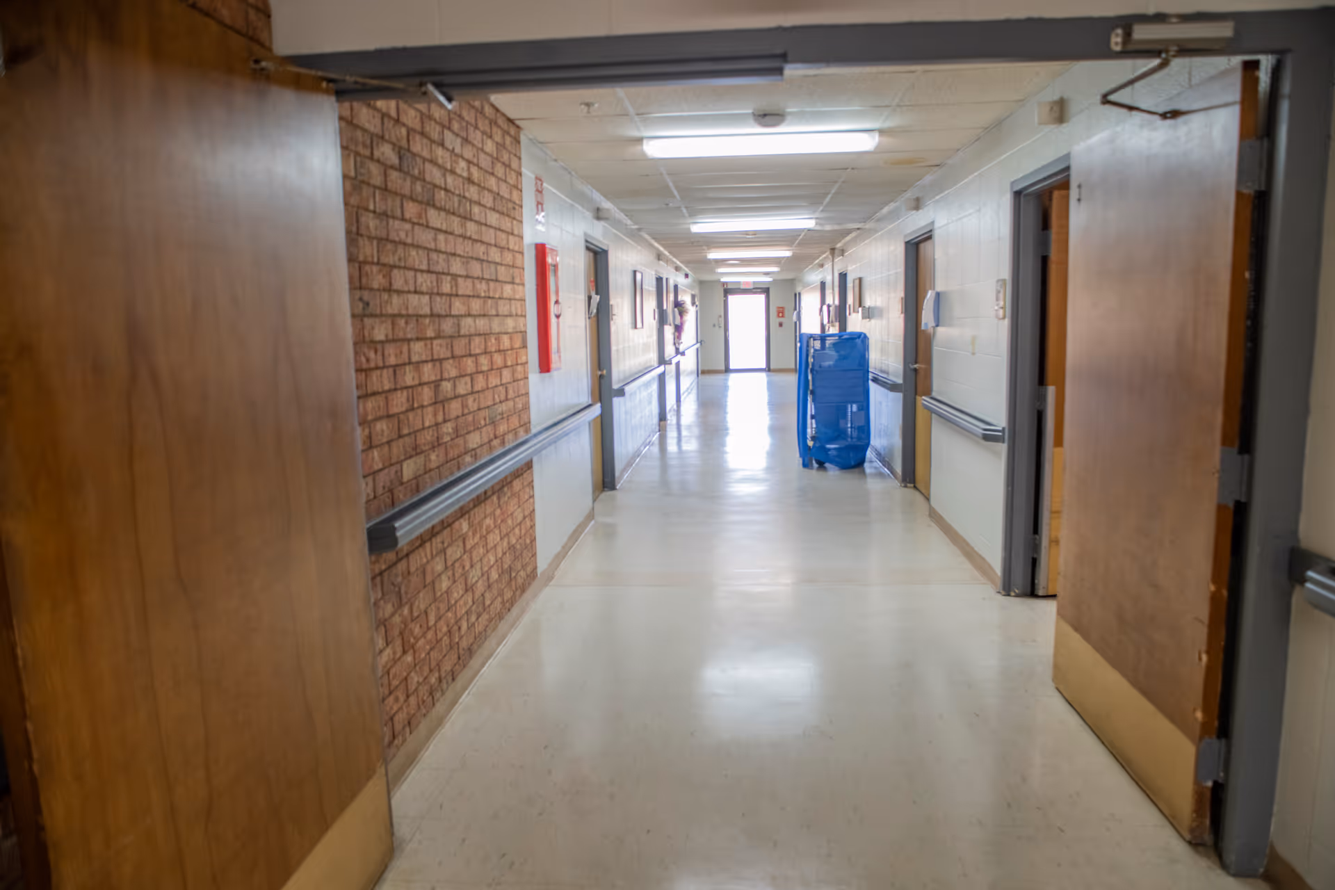 Long interior hallway at a senior living facility with brick wall and closed doors.