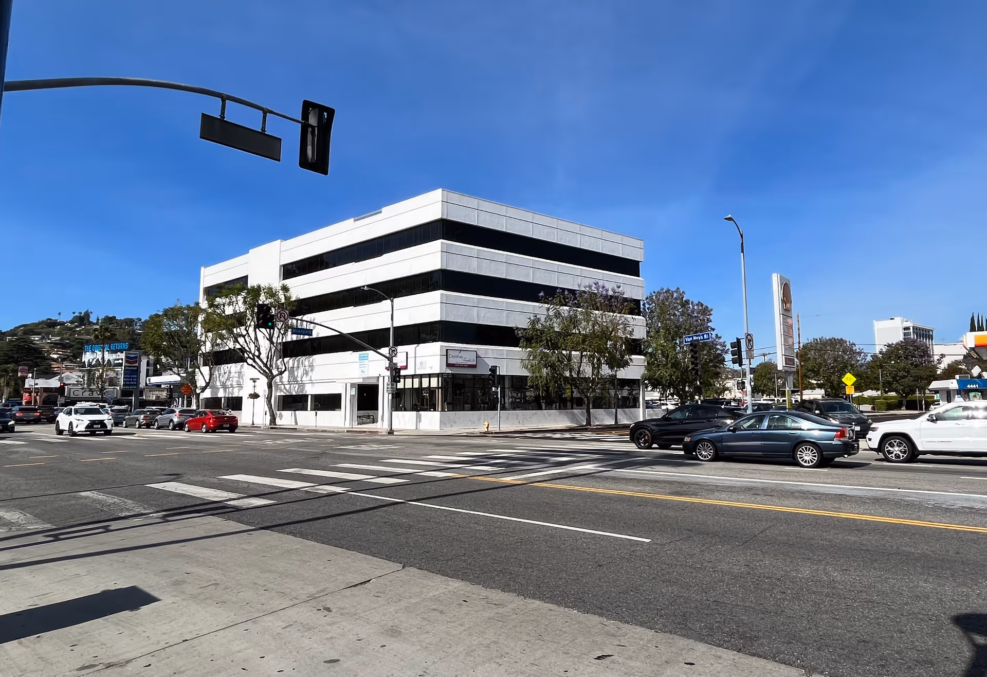 A modern white building on a busy street corner with a crosswalk and parked cars.