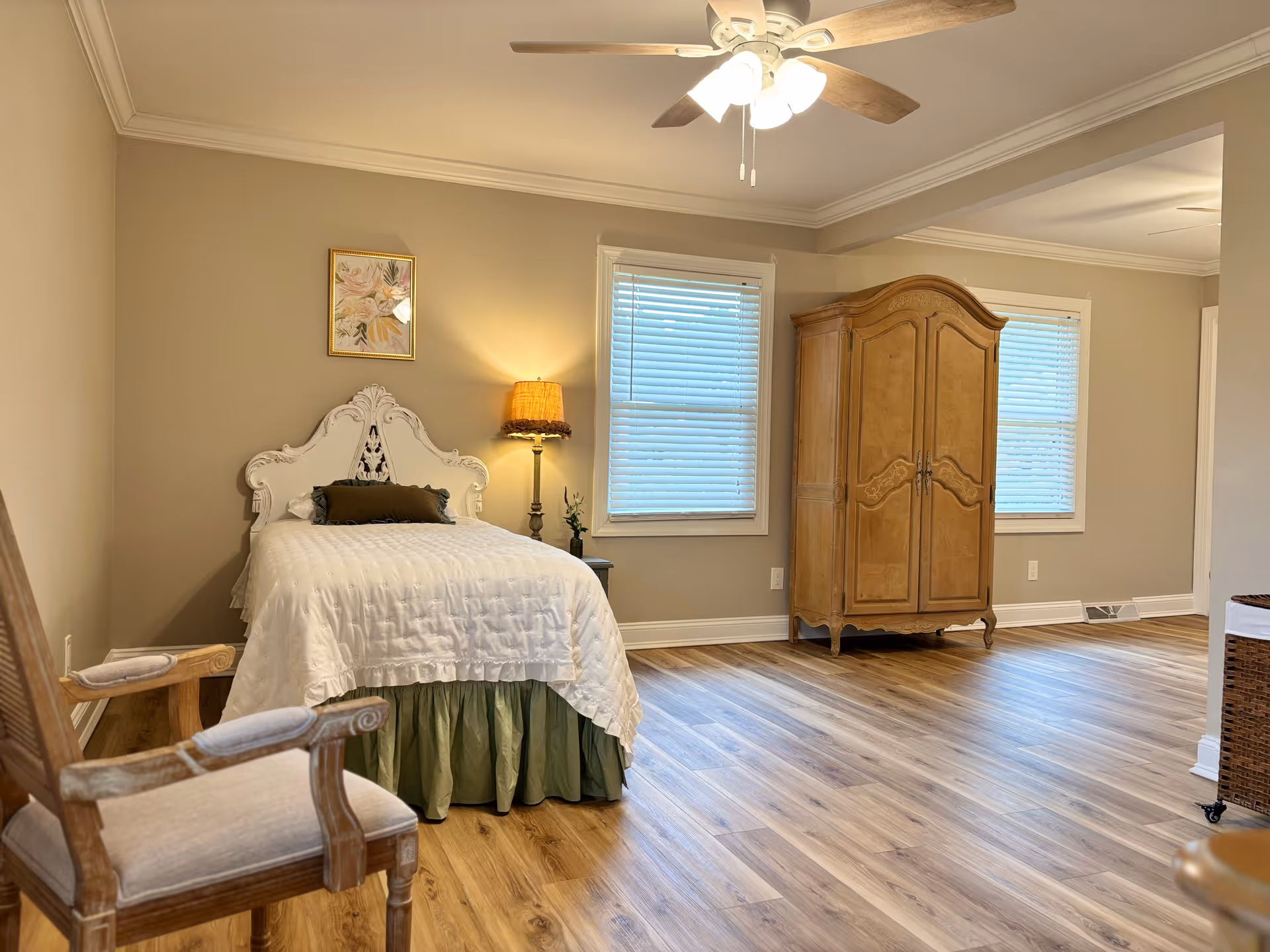 Bedroom featuring an ornate white headboard bed, wooden armoire, chair, and wood flooring.