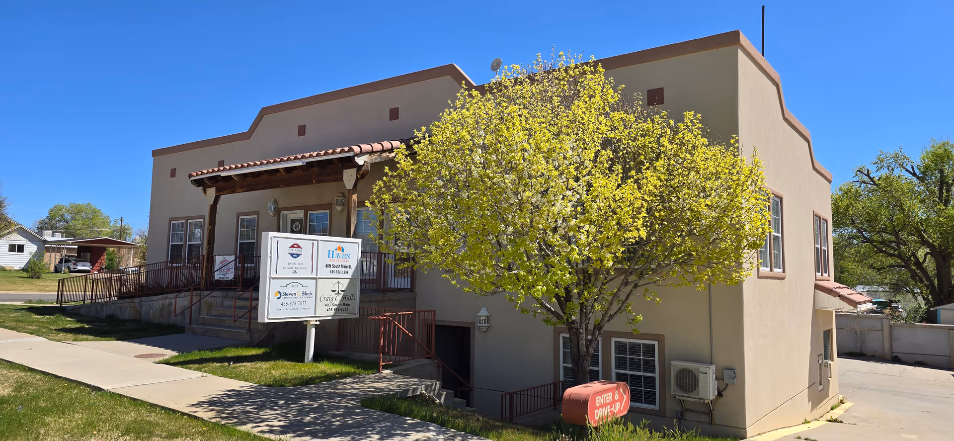 Beige two-story senior care building with a tree, sign, and walkway in front.