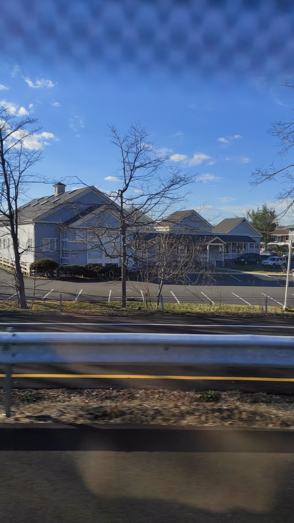 Blue, single-story senior living facility with parking along a road and leafless trees.