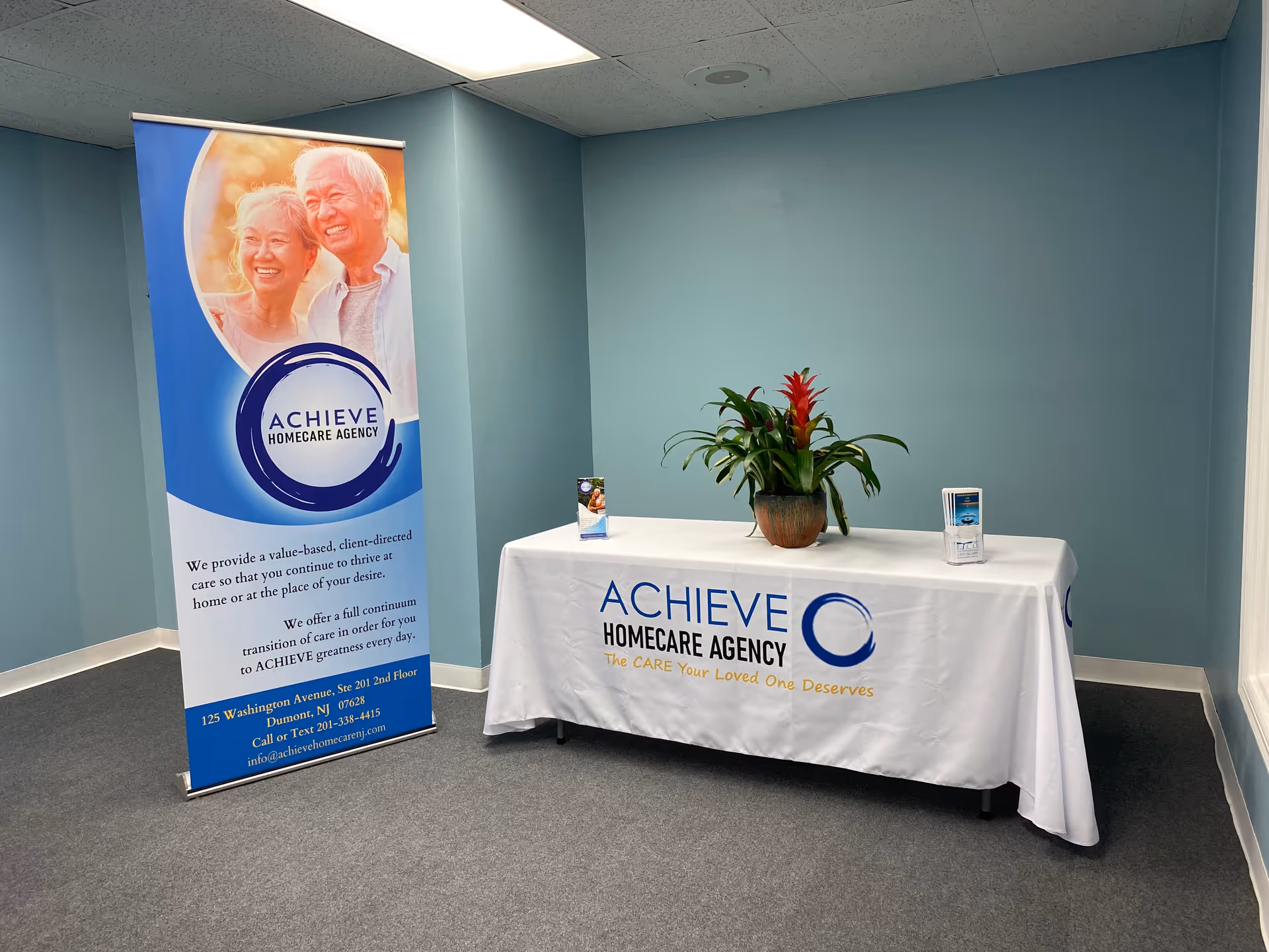 Indoor reception area with ACHIEVE Homecare Agency banner and a table with a plant.