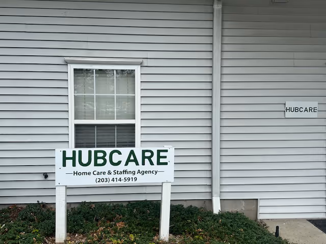 Exterior view of a light-gray building with HUBCARE sign and front yard.