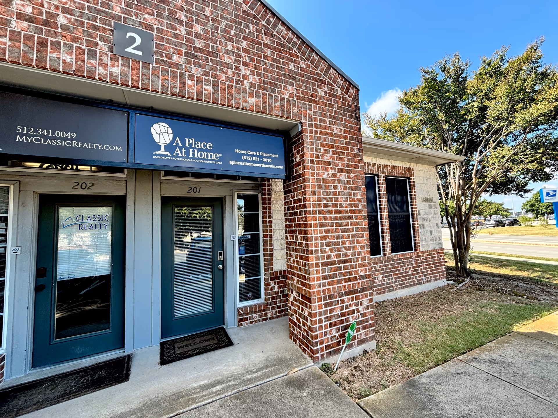 Brick storefront with two glass doors labeled 201 and 202 under A Place At Home signage.