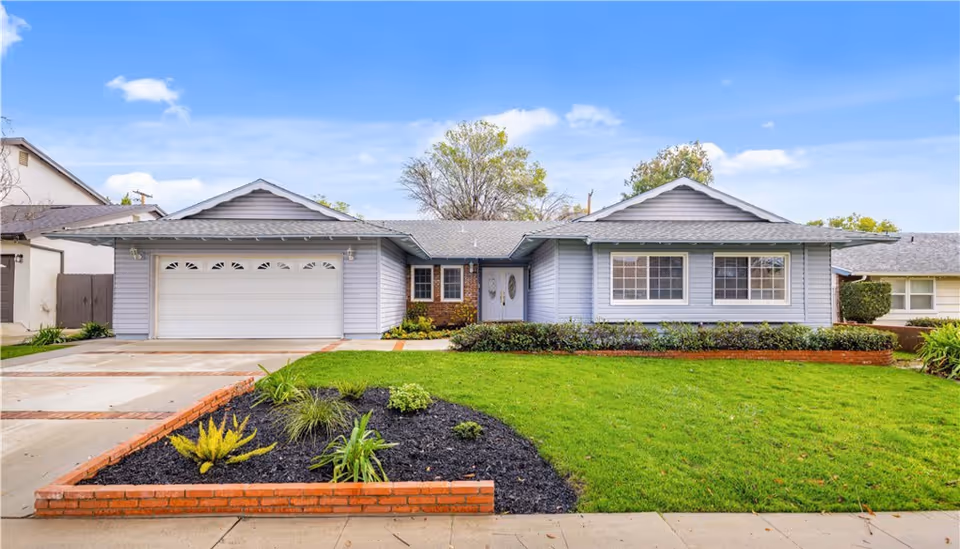 Single-story ranch-style house with an attached two-car garage, manicured lawn and brick-bordered flower beds in front.