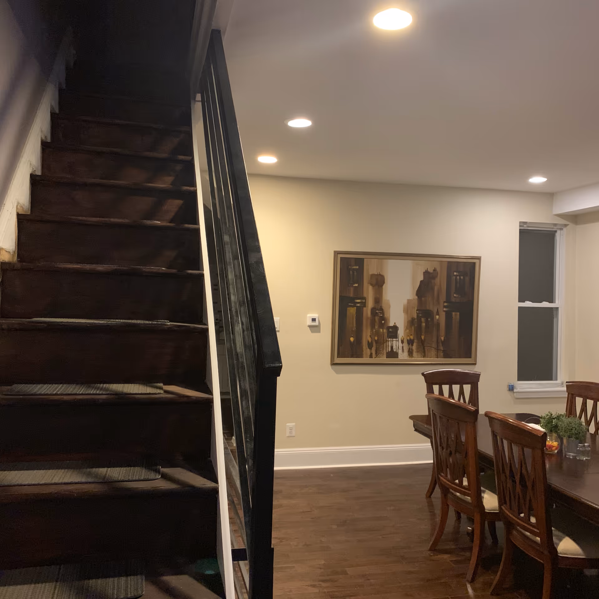 Interior dining area with wooden table, chairs, staircase, and wall art.