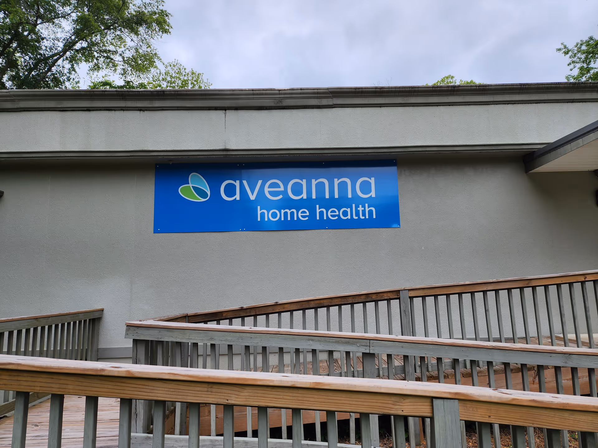 Exterior view of Aveanna Home Health building with a blue sign and wooden railing.