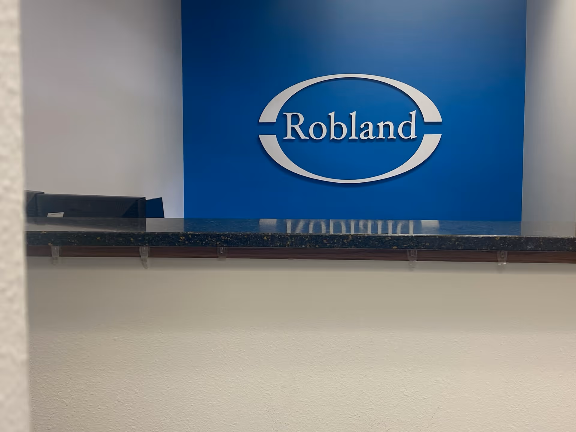 Reception desk in a lobby featuring a blue wall and a large Robland logo.