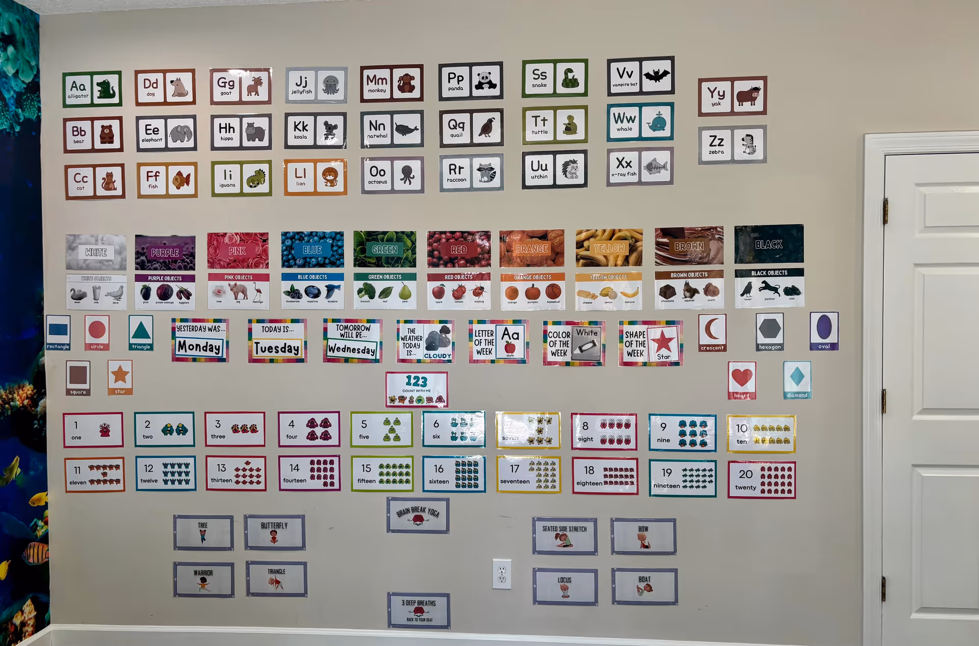 Classroom-style wall display of alphabet cards, numbers, and shapes in a facility interior.