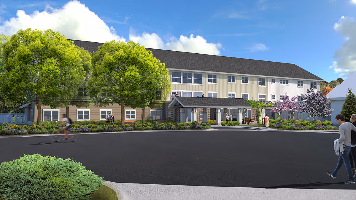 Front exterior of a three-story senior living facility with a covered entrance, landscaped grounds, large trees, and people walking and biking in the foreground.