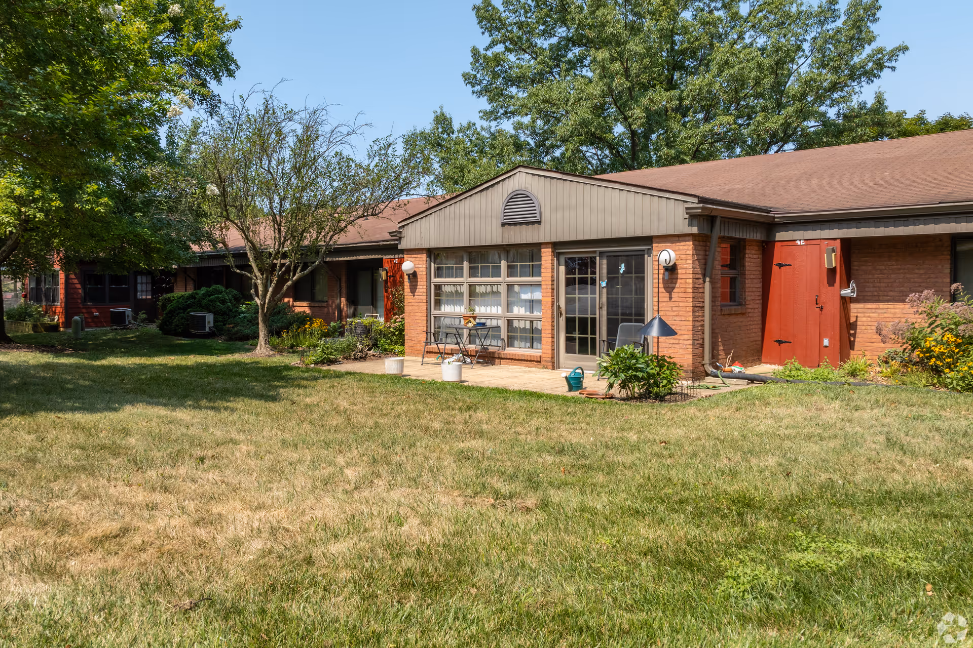 Exterior of Heritage at Augsburg, brick building with large windows, lawn, trees, and a small patio.