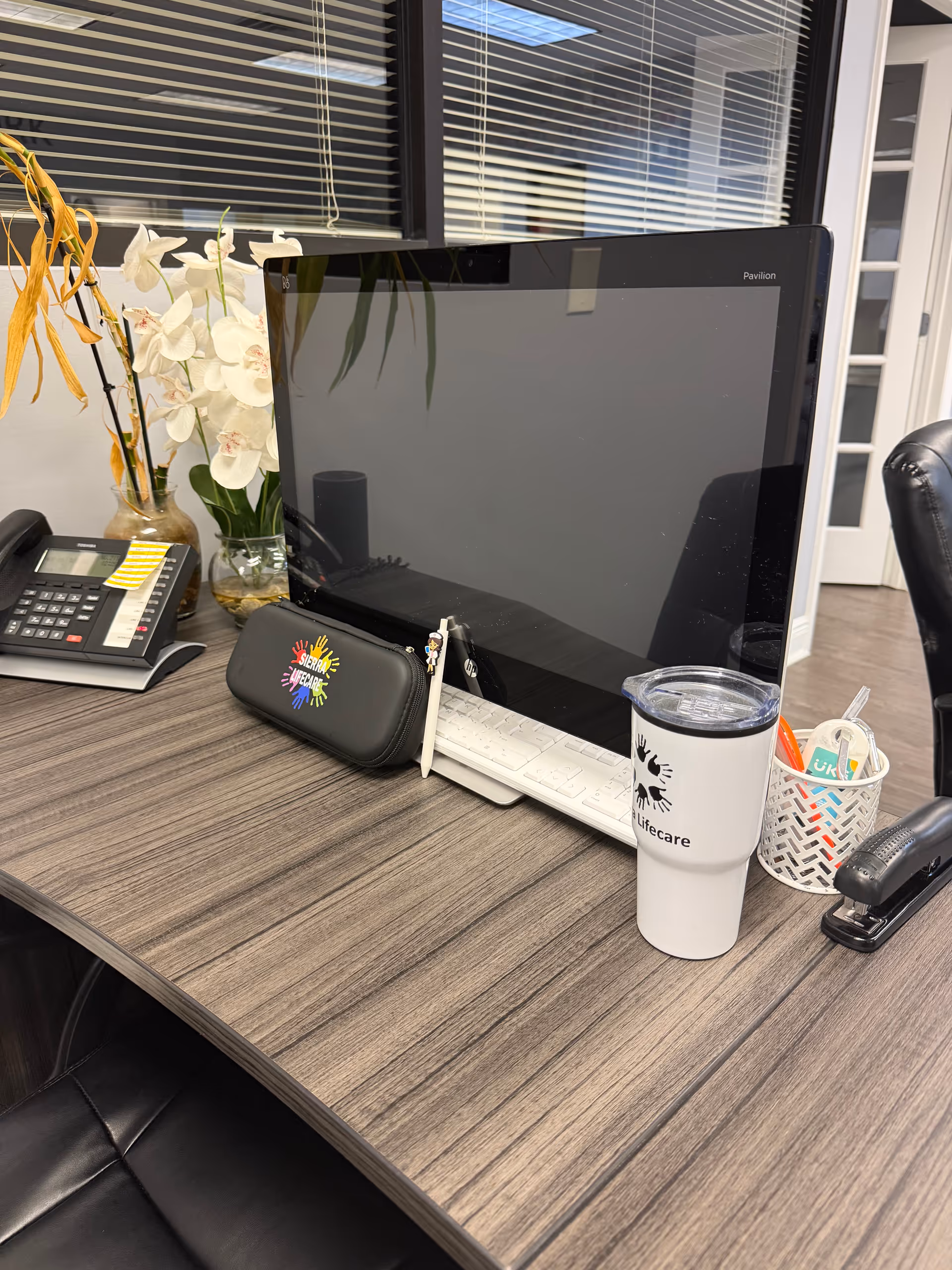 Desk with computer monitor, phone, and branded tumbler in a Sierra Lifecare office.