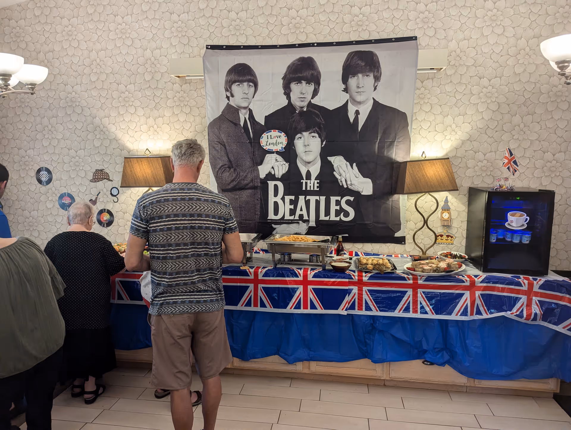 Residents line up at a Beatles-themed buffet in a Union Jack adorned dining area.