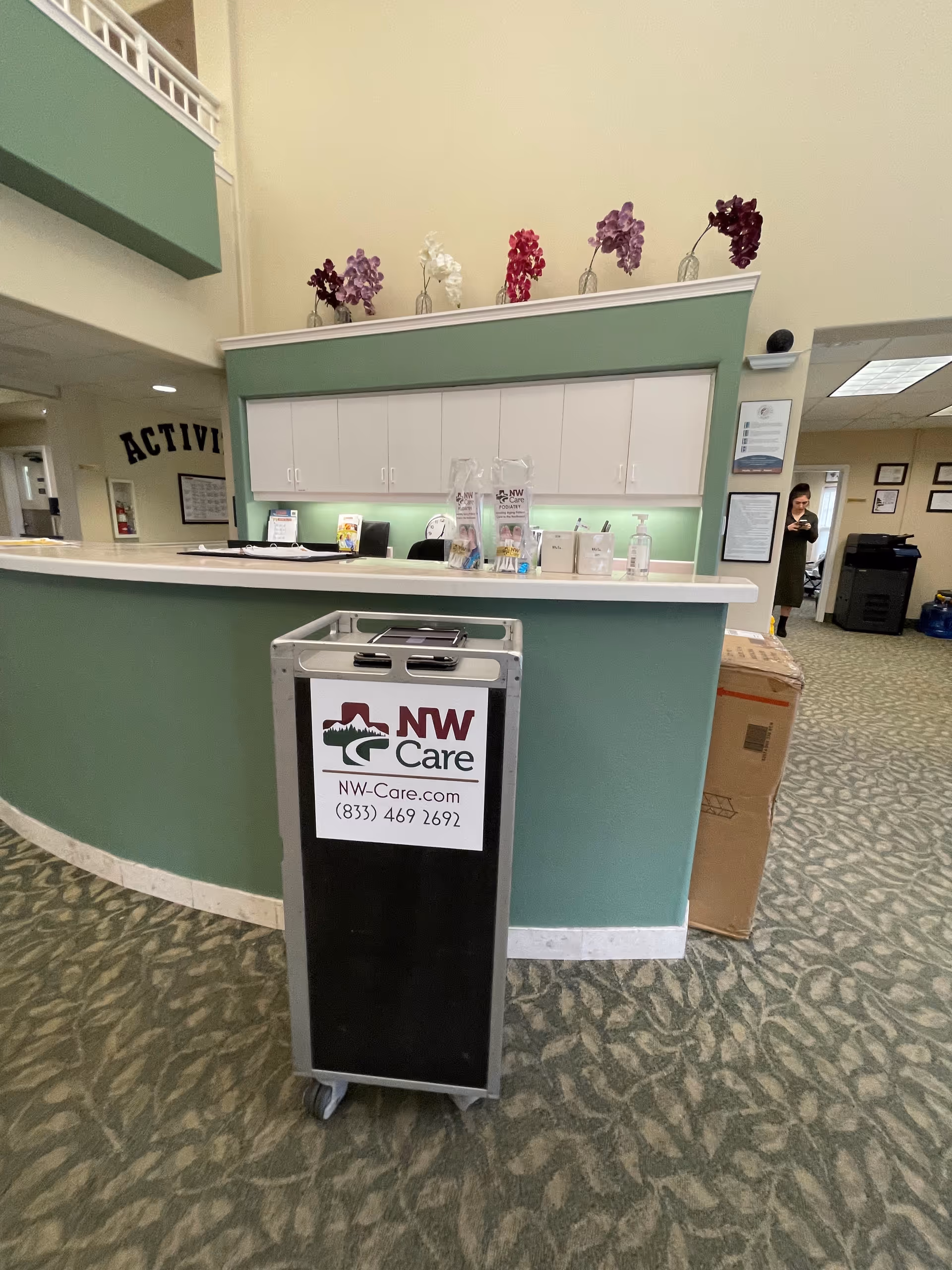 Reception desk with a green counter and NW Care branding in a lobby.