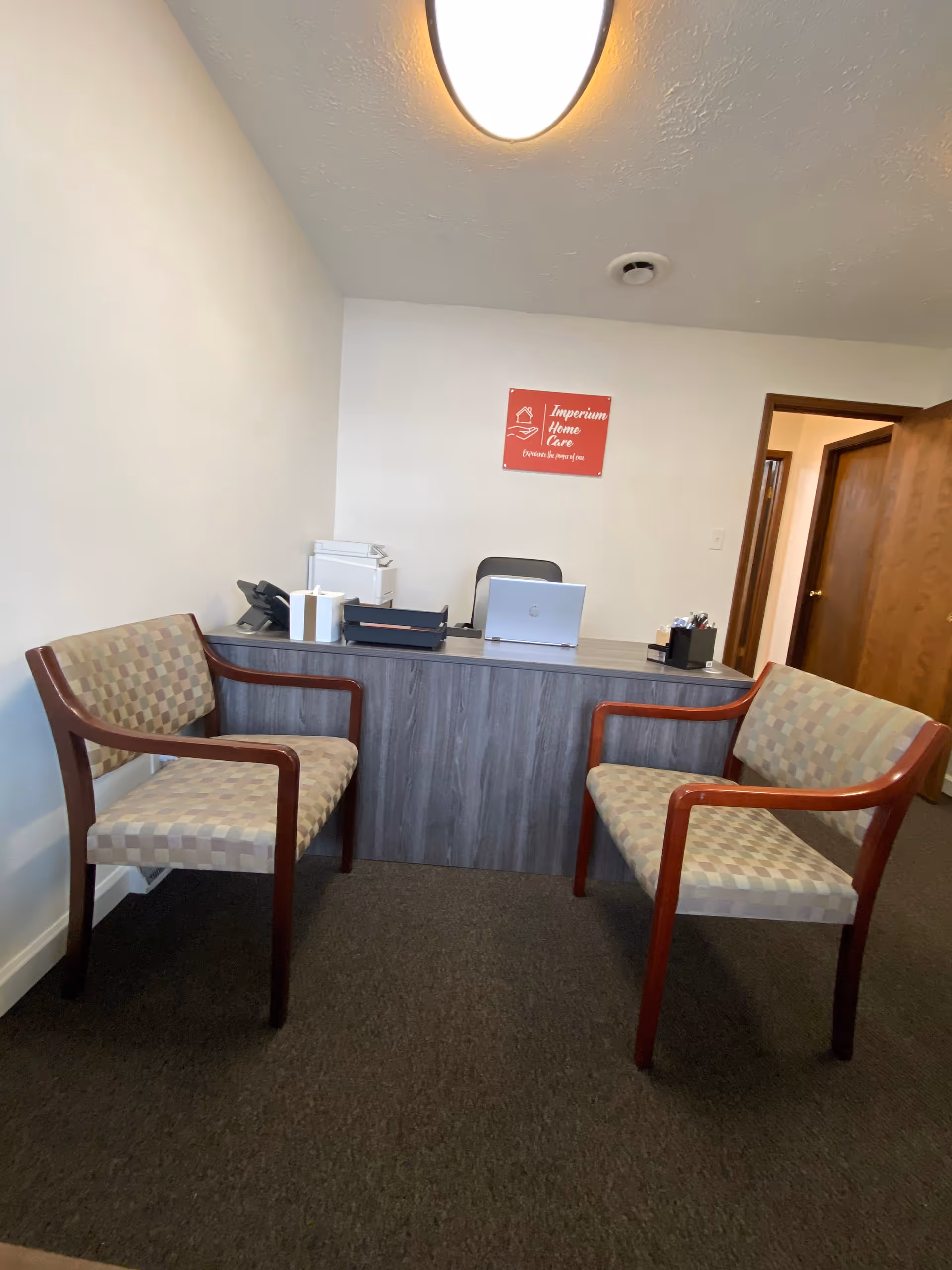 Reception desk with laptop and two patterned chairs in a small Imperium Home Care office.